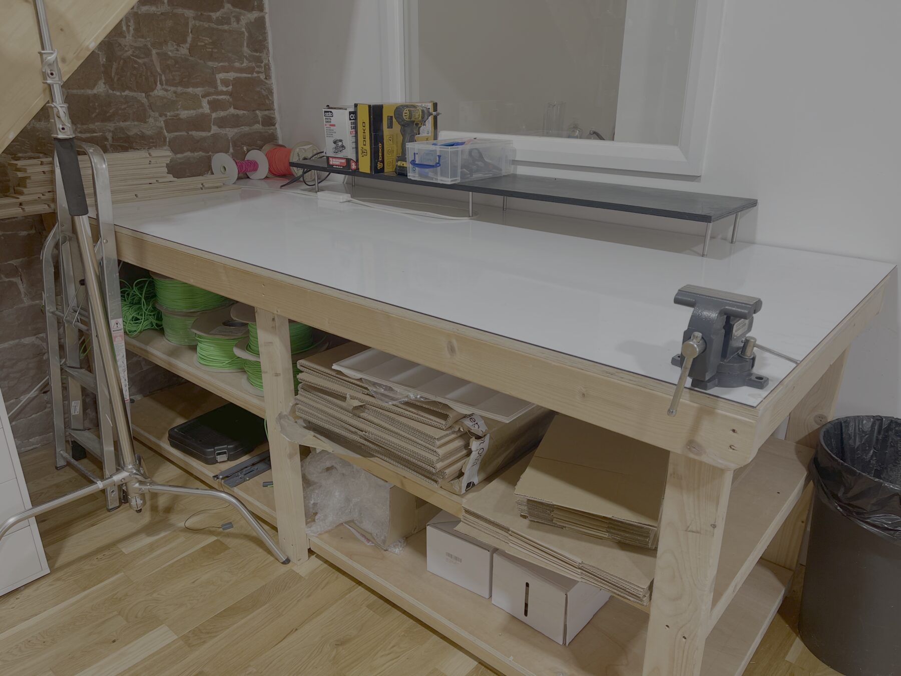 The workshop area at Lake District Film Studios: a timber workbench with a bench vice, shelves of offcuts, tape and boxes underneath, and a folded C-stand against the exposed stone wall