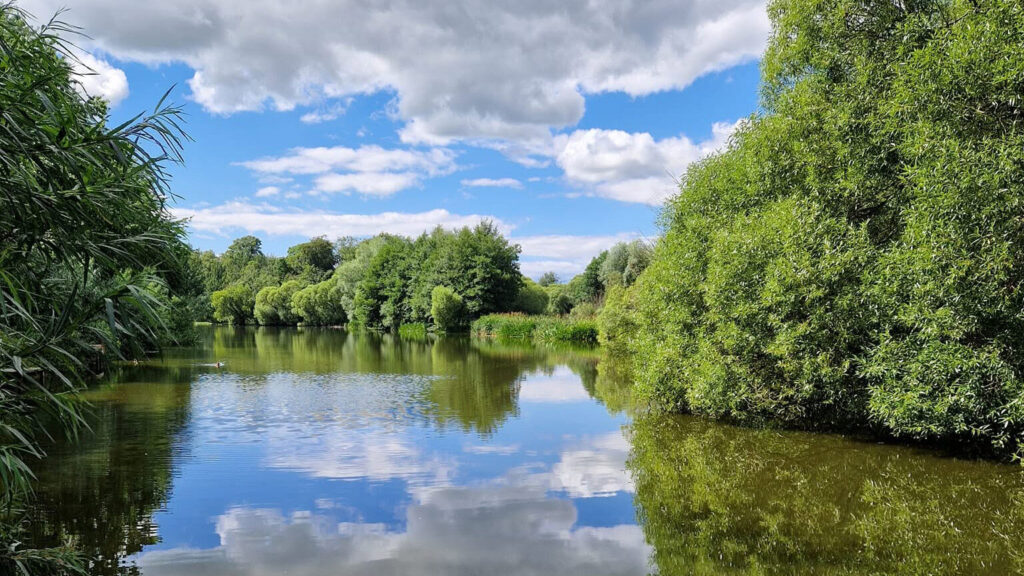 The lake at Crofton Hall, still water reflecting cloud and summer trees, a few minutes from Lake District Film Studios